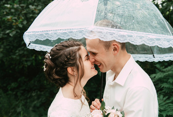 Happy bride and groom stand with a transparent wedding umbrella