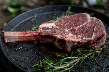 tomahawk steak raw on grilling pan with rosemary