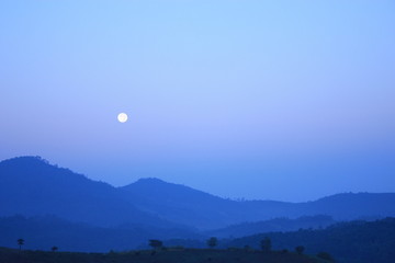 The moon in the morning on the blue sky with the mountains when sun rise.
