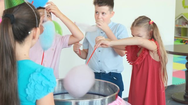 children eat tasty cotton candies near modern machine in room decorated with balloons at birthday party slow motion