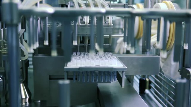 Fully automated equipment is producing coVID-19 vaccines, with liquid being pumped into glass bottles