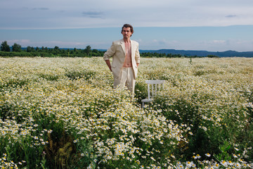 Tall handsome man standing in camomile flowers field
