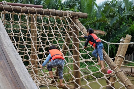 Two cute young Asian girls wearing orange life vest are going up a climbing net in an obstacle course at a summer camp. - Powered by Adobe