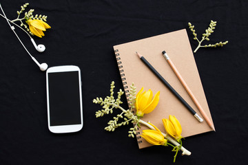 notebook planner ,mobile phone for business work with yellow flower ylang ylang arrangement flat lay style on background black