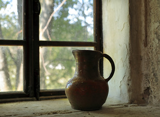 Still life with an old clay jug on the window in an abandoned house.