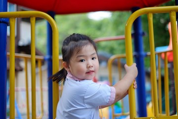 A cute young Asian girl in school uniform is climbing up a jungle gym at the school playground during recess hour.