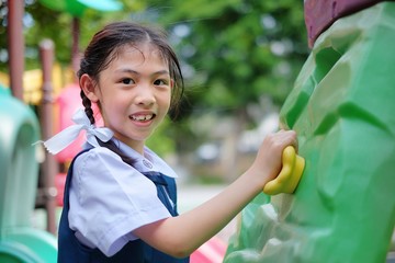 A cute young Asian girl in white and blue school uniform is playing rock climbing at a playground, exercising and having fun.