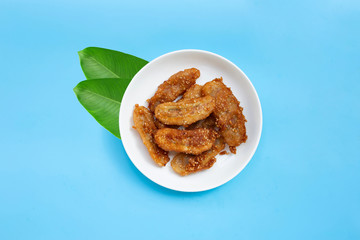 Fried bananas with sesame seeds on white ceramic round plate on blue background. Top view with copy space