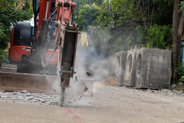 Hydraulic jackhammer from excavator construction truck drilling concrete ground with flying...