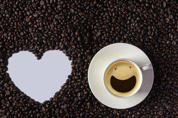 Top view of smiley face from espresso coffee bubbles shown in white coffee cup and put on group of many coffee beans with white heart shaped for copy space. Background for International Coffee Day.