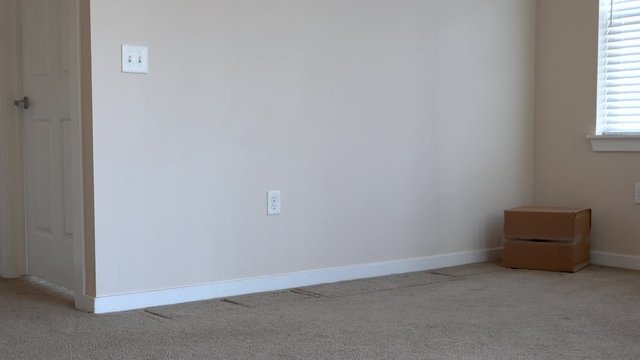 Senior man dressed casually drop kicks a cardboard moving box across an empty apartment room.