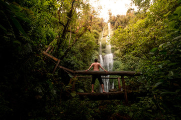 Hombre en puente de madera observando una cascada en medio de la naturaleza