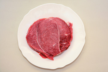 Raw beef meat steak on white plate on light background. Carnivore, keto