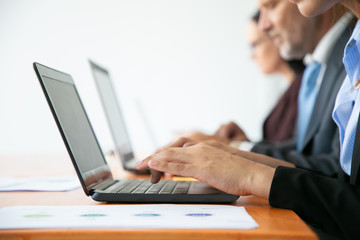 Row of business people working at computers. Hands of employees typing on laptop keyboards. Side view, closeup, cropped shot. Communication or wireless technology concept