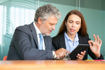 Businesswoman presenting project to investor. Serious female employee showing content on tablet to colleague, explaining details. Communication or teamwork concept