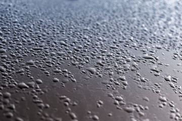 The surface of the car's body is covered with drops of water during the rain.