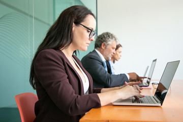 Group of business people sitting in line and using computers in office. Employees of different ages typing on laptop keyboards. Side view, closeup. Communication or wireless technology concept