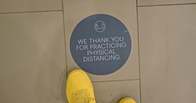 Tourist steps on floor sign at hotel reminding to keep 6 feet social distance. Man in yellow sneakers is walking in the hotel lobby by social distancing signage. Safe travels under COVID-19, 4K USA