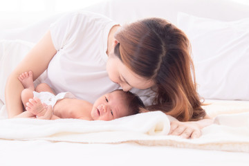 Obraz na płótnie Canvas Beautiful happy Asian women mom kissing healthy toddler newborn baby in bed at home, Healthcare medical lifestyle mother's day/ young motherhood concept, infant sleep safe and protection in mom's arm