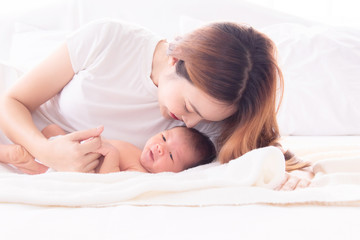 Obraz na płótnie Canvas Beautiful happy Asian women mom kissing healthy toddler newborn baby in bed at home, Healthcare medical lifestyle mother's day/ young motherhood concept, infant sleep safe and protection in mom's arm