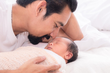 Obraz na płótnie Canvas Handsome happy Asian men with beard dad kissing healthy toddler newborn baby in bed at home, Healthcare medical lifestyle father day/ parenthood concept, infant sleep safe and protection bonding