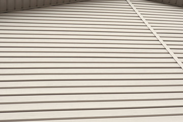 The striped surface of the plastic siding and a piece of cornice. Construction and repair of buildings. Light brown or beige background or wallpaper. Building material and technologies