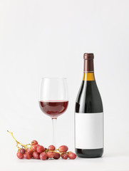 Bottle of wine with blank label, glass and grapes on light background