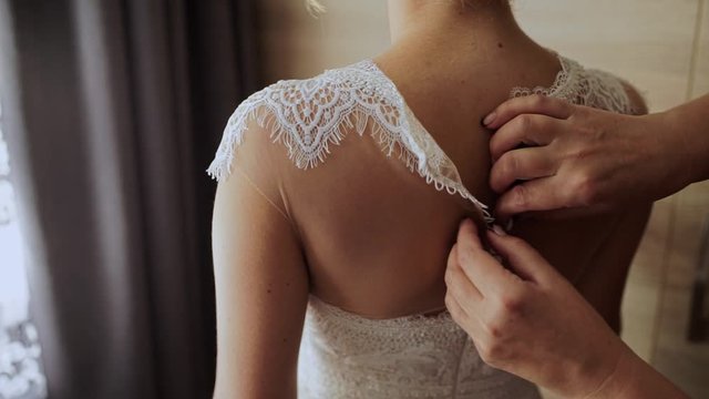 bride buttoning wedding dress on the back
