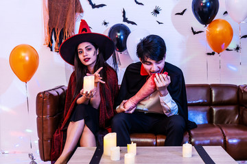 Asian Happy friends sitting on sofa in costumes and makeup on a celebration of Halloween posing Eat fake human legs in party, Group of young people enjoying Halloween party at home or nightclub.