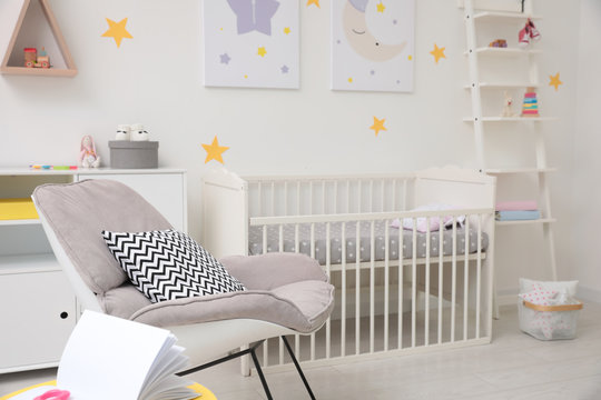 Stylish baby room interior with crib and armchair