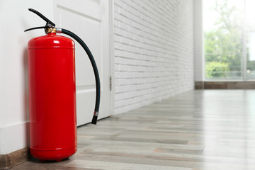 Fire extinguisher on floor near door indoors, space for text