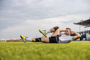 Handsome unshaven soccer player in shape doing sit-ups on the field.