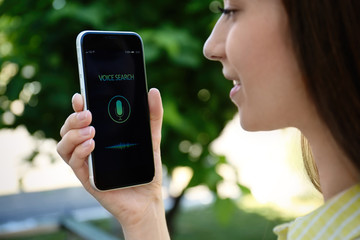 Woman using voice search on smartphone outdoors, closeup