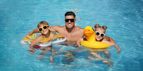 Happy man and his children with inflatable rings in outdoor swimming pool on sunny summer day