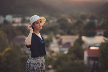 An elegant woman holds her hat in her hand and poses in a half-turn. Side view. In the background, a view of the city. Copy space. Travel and leisure concept