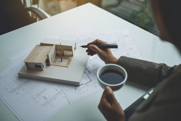 A female architect working on an architecture house model with shop drawing paper in the office