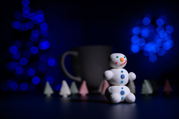 Cute snowman and little Christmas trees made of marshmallows on the background of Christmas lights....