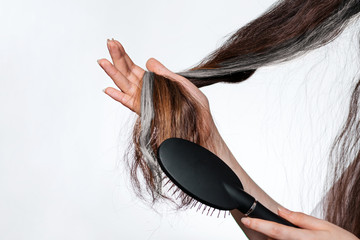 A woman holds a gray lock of hair and combs it. Close up of hands. The concept of hair care and gray hair coloring