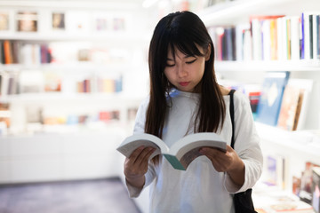 Young female student choosing new books on shelves in library