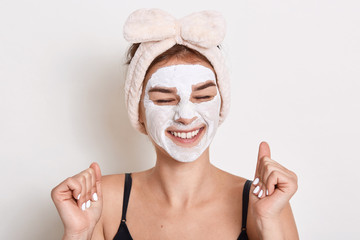 Photo of glad satisfied woman keeps eyes closed with toothy smile, has cosmetic procedures at home,...