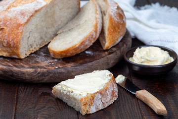 Piece of fresh backed Classic Boule bread with butter on wooden table, horizontal