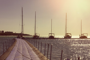 Several yachts in a row are parked at the pier. Sunset sky and sea in the background. Sunlight