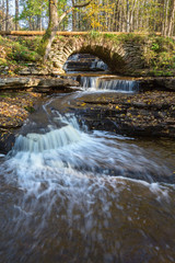 Stream in a canyon with waterfalls and an old arch bridge