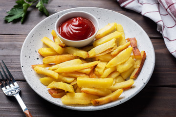 Fried French fries potatoes with tomato ketchup sauce on a plate. Wooden background. Copy space.