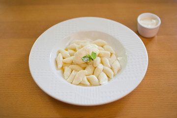Lazy dumplings - vareniki of cottage cheese on a white plate served with sour cream sauce, top view close up on wooden background