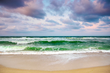 dramatic weather on the seashore. green waves crashing on the beach. cloudy purple sky in evening light