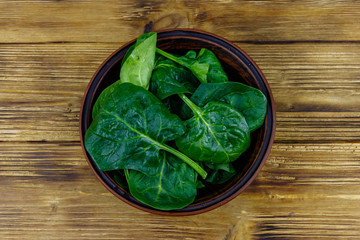 Fresh green spinach leaves in bowl on a wooden table. Top view