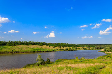 Summer landscape with beautiful lake, green meadows, hills, trees and blue sky