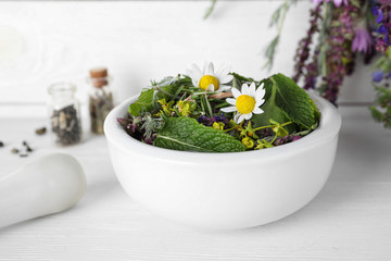 Mortar with healing herbs and pestle on white wooden table, closeup