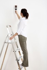 Woman standing on ladder painting the wall